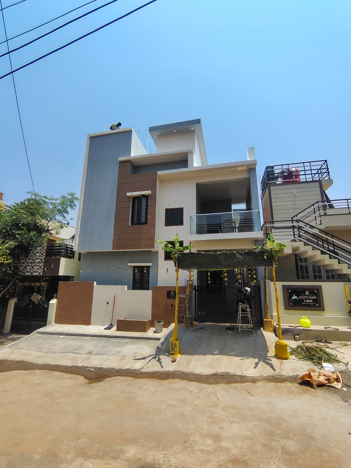 Three-storey residence under finishing works, with grey and brown facade panels and a decorated entrance for housewarming